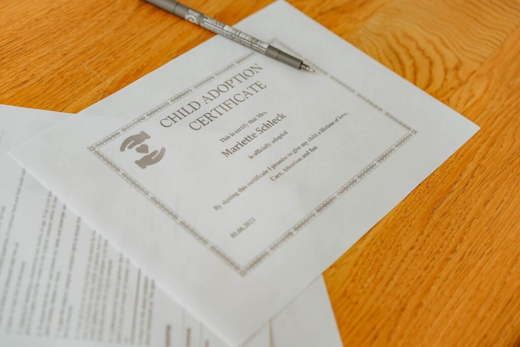 Close-up of a child adoption certificate and documents with a pen on a wooden table.